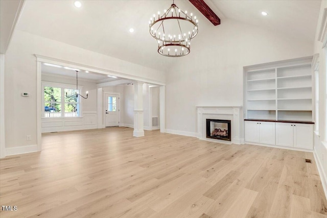 unfurnished living room with a notable chandelier, light wood-type flooring, lofted ceiling with beams, and a premium fireplace