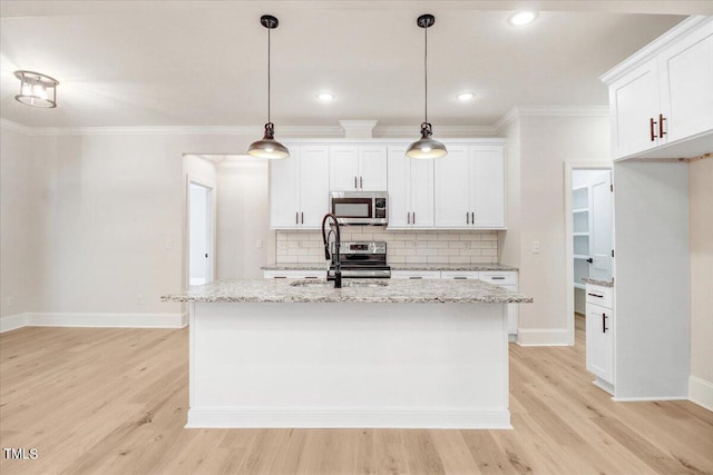 kitchen with appliances with stainless steel finishes, hanging light fixtures, white cabinets, light stone countertops, and a center island with sink