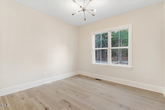 spare room featuring a notable chandelier and light wood-type flooring