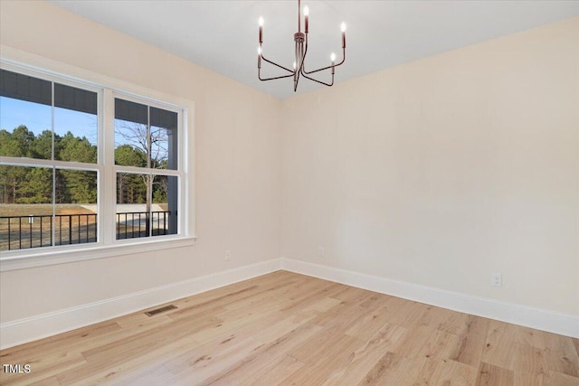 spare room featuring a notable chandelier and light hardwood / wood-style flooring