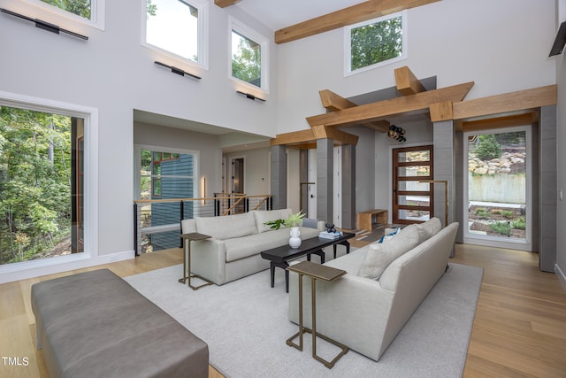 living room with light wood-type flooring, a towering ceiling, beamed ceiling, and a wealth of natural light