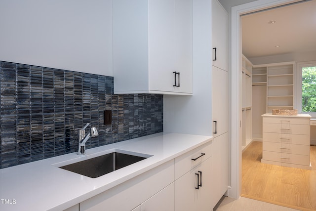 kitchen with light wood-type flooring, backsplash, white cabinetry, and sink