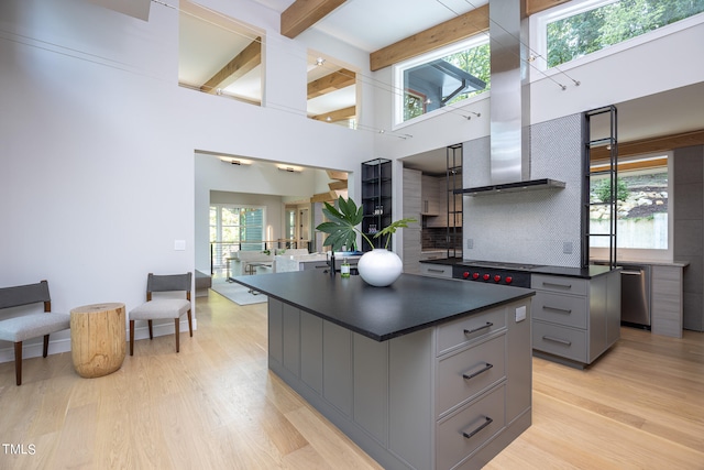 kitchen with a towering ceiling, backsplash, a kitchen island, gray cabinets, and range hood