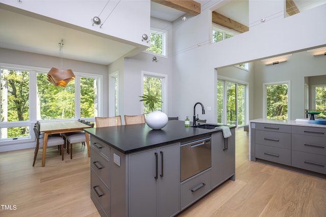 kitchen featuring light hardwood / wood-style floors, a towering ceiling, an island with sink, gray cabinets, and decorative light fixtures