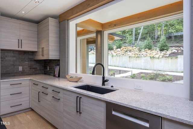 kitchen featuring light stone counters, sink, tasteful backsplash, stainless steel dishwasher, and light wood-type flooring