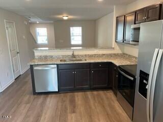 kitchen featuring dark brown cabinetry, sink, light hardwood / wood-style floors, kitchen peninsula, and appliances with stainless steel finishes