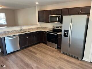 kitchen with appliances with stainless steel finishes, dark brown cabinetry, and light hardwood / wood-style floors