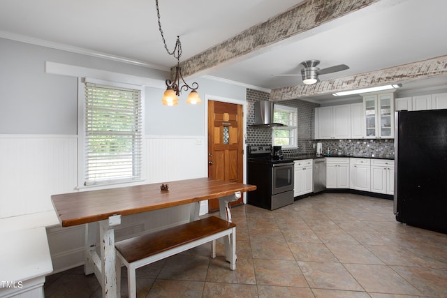 kitchen with pendant lighting, ceiling fan with notable chandelier, white cabinets, wall chimney exhaust hood, and appliances with stainless steel finishes