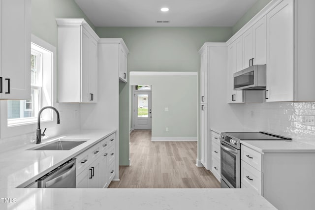 kitchen with appliances with stainless steel finishes, light hardwood / wood-style floors, white cabinetry, light stone counters, and sink