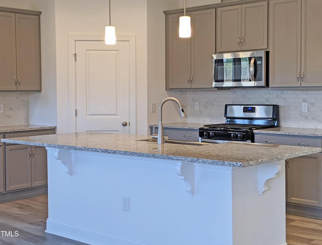 kitchen featuring appliances with stainless steel finishes, hanging light fixtures, light hardwood / wood-style floors, an island with sink, and sink