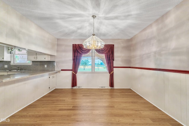 unfurnished dining area featuring a textured ceiling, sink, light hardwood / wood-style flooring, and a chandelier