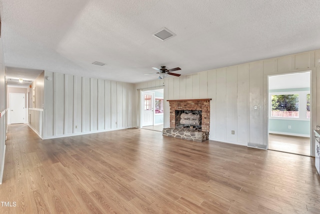 unfurnished living room with a brick fireplace, light hardwood / wood-style floors, ceiling fan, and a textured ceiling