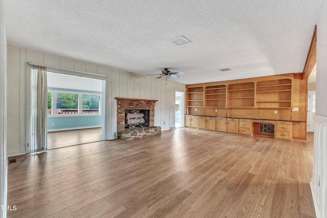 unfurnished living room featuring light hardwood / wood-style flooring, a brick fireplace, ceiling fan, and a textured ceiling