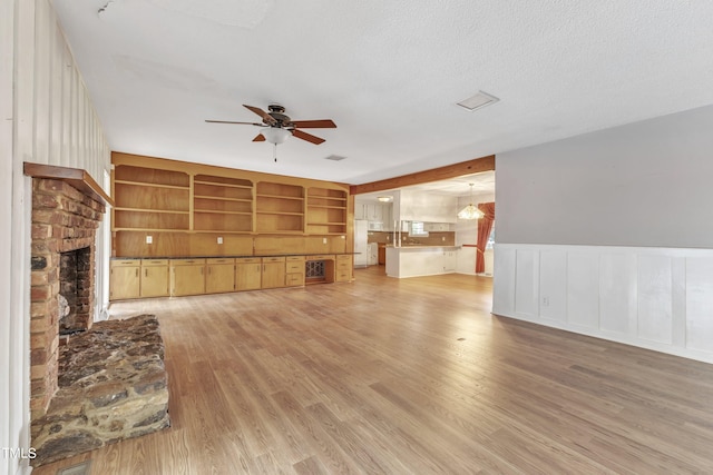 unfurnished living room with ceiling fan with notable chandelier, a brick fireplace, light hardwood / wood-style floors, and a textured ceiling