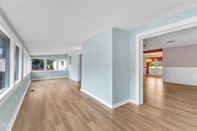 spare room with a textured ceiling, light hardwood / wood-style flooring, and vaulted ceiling