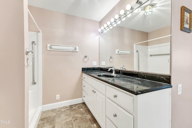 bathroom with a textured ceiling, vanity, and walk in shower