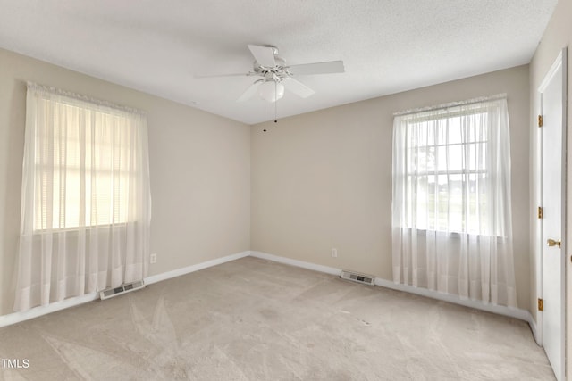 carpeted empty room with ceiling fan, plenty of natural light, and a textured ceiling