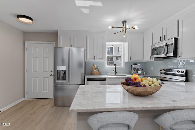 kitchen with sink, a chandelier, white cabinetry, appliances with stainless steel finishes, and light hardwood / wood-style floors