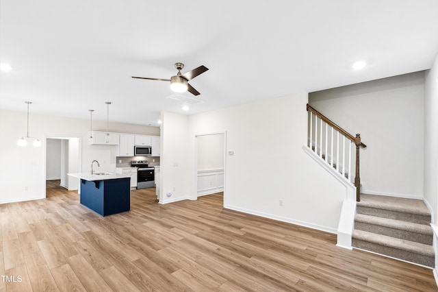 kitchen featuring appliances with stainless steel finishes, sink, white cabinets, hanging light fixtures, and a center island with sink
