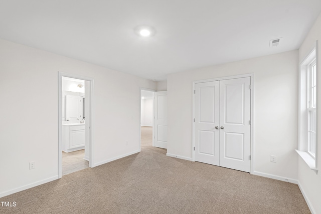 unfurnished bedroom with connected bathroom, light colored carpet, and a closet