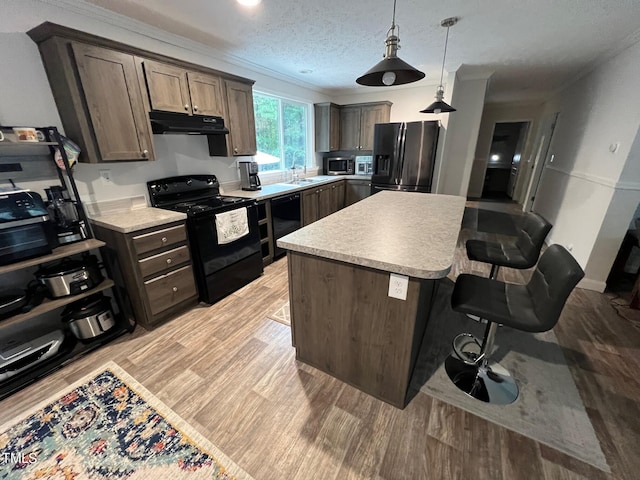 kitchen featuring light hardwood / wood-style floors, a textured ceiling, black appliances, a kitchen bar, and a center island