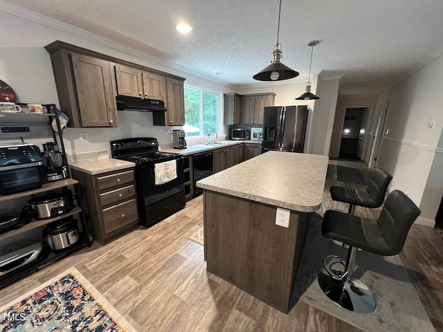 kitchen featuring light wood-type flooring, a textured ceiling, a kitchen bar, a kitchen island, and black appliances