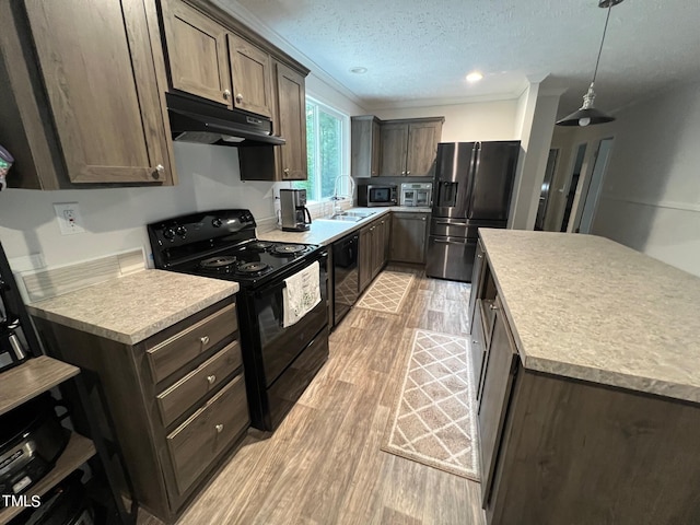 kitchen featuring light hardwood / wood-style flooring, black appliances, decorative light fixtures, and crown molding