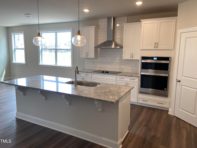 kitchen featuring wall chimney exhaust hood, light stone counters, pendant lighting, black electric cooktop, and white cabinets