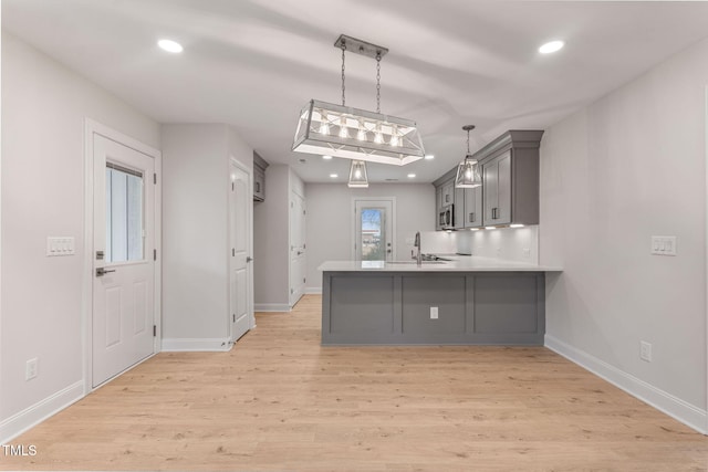 kitchen featuring kitchen peninsula, a kitchen bar, gray cabinetry, pendant lighting, and light hardwood / wood-style flooring