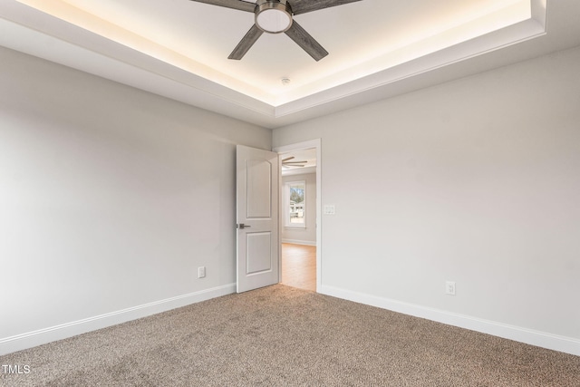 empty room featuring a tray ceiling, ceiling fan, and carpet floors