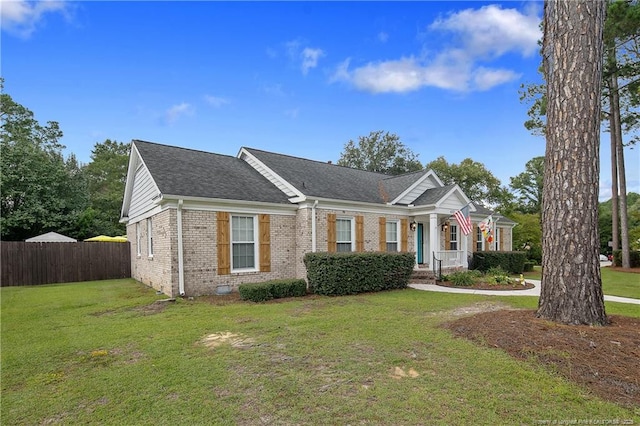 view of front facade featuring a shingled roof, a front yard, fence, and brick siding