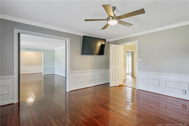 empty room with dark wood-style floors, ceiling fan, crown molding, and a wainscoted wall