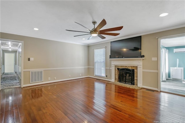 unfurnished living room with a fireplace, wood finished floors, visible vents, baseboards, and an AC wall unit