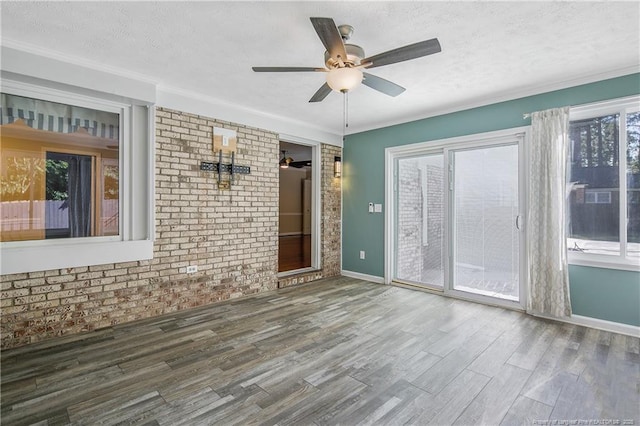 empty room featuring baseboards, brick wall, ceiling fan, wood finished floors, and a textured ceiling