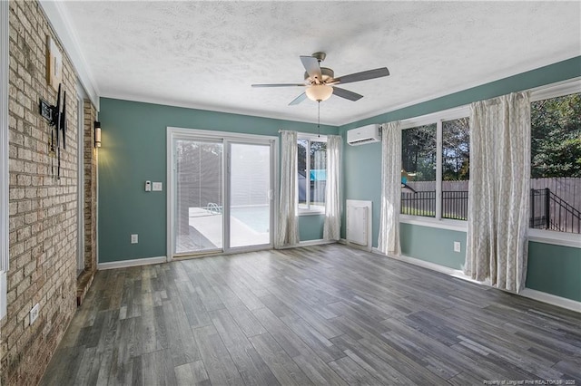 spare room with a textured ceiling, an AC wall unit, dark wood finished floors, and a healthy amount of sunlight