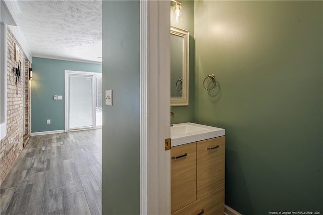 bathroom with wood finished floors, a textured ceiling, brick wall, vanity, and baseboards