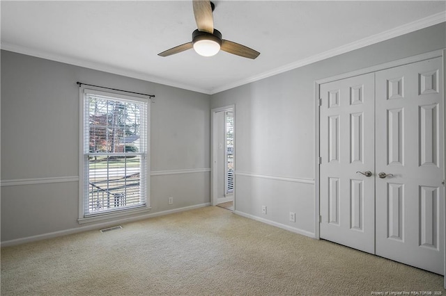 spare room with light colored carpet, visible vents, ornamental molding, a ceiling fan, and baseboards