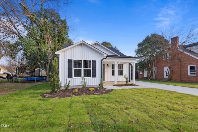 view of front of house with covered porch, a trampoline, and a front yard