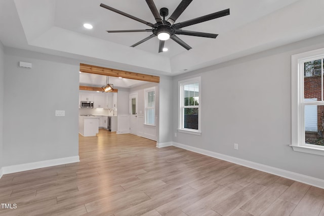 unfurnished living room with ceiling fan, a healthy amount of sunlight, and a tray ceiling