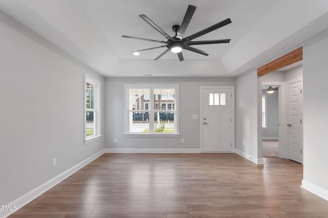 entryway with a raised ceiling, ceiling fan, and light wood-type flooring