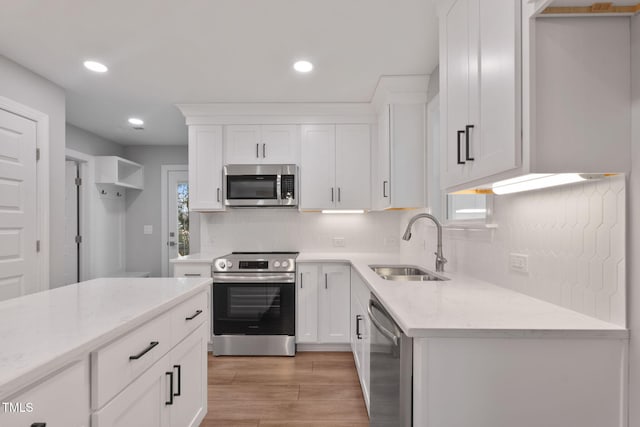 kitchen featuring light stone countertops, white cabinetry, sink, stainless steel appliances, and light wood-type flooring