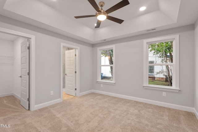 unfurnished bedroom featuring light colored carpet, a raised ceiling, a walk in closet, and multiple windows