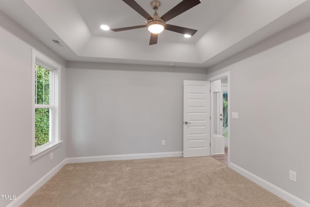 carpeted empty room with a raised ceiling and ceiling fan