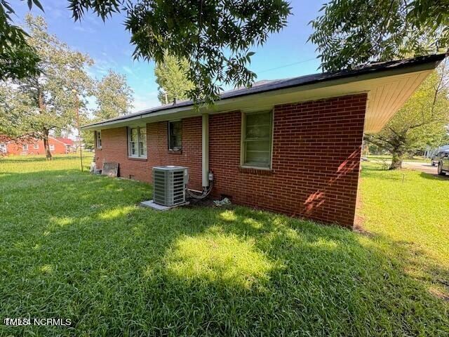 rear view of house featuring central AC unit and a lawn