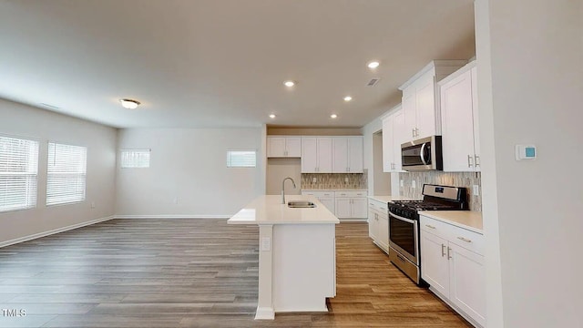 kitchen featuring light wood-type flooring, a kitchen island with sink, stainless steel appliances, white cabinets, and sink