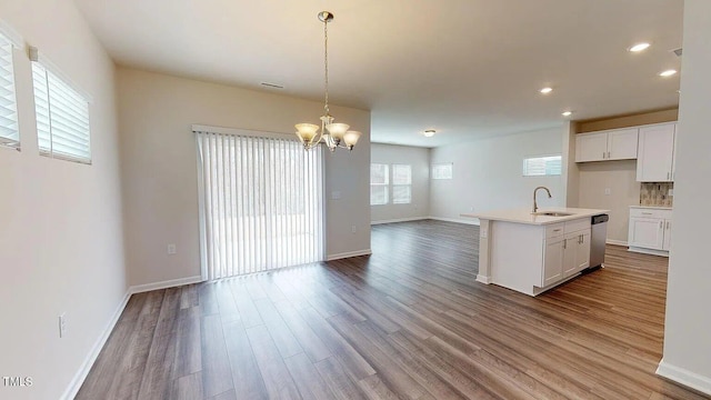 kitchen featuring an island with sink, white cabinets, decorative light fixtures, and light wood-type flooring