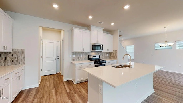 kitchen with light wood-type flooring, sink, pendant lighting, white cabinetry, and appliances with stainless steel finishes