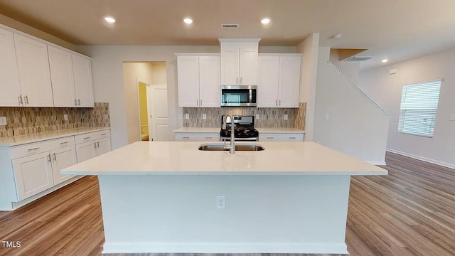 kitchen with light hardwood / wood-style flooring, sink, stainless steel appliances, an island with sink, and white cabinetry