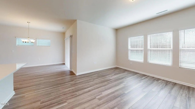 empty room with light wood-type flooring and a notable chandelier