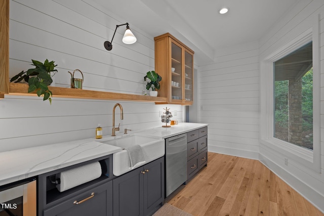 bar with wood walls, light wood-type flooring, light stone counters, sink, and stainless steel dishwasher